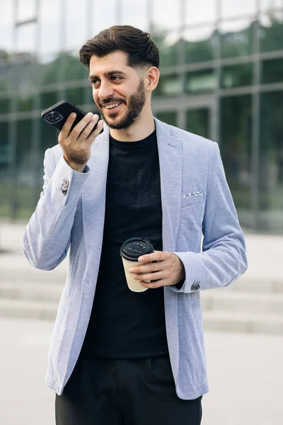 Bearded millennial businessman entrepreneur talk on speakerphone with friend make voice recognition use virtual assistant digital application record audio message on mobile app.