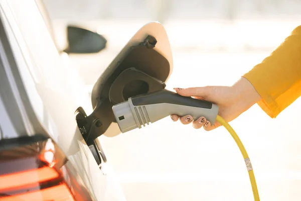 Close up shot of a womans hands plugging in her electric car or EV at electric charging station. Electric vehicle charging port plugging in EV modern car. Save ecology of future.