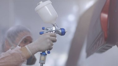 Araba servisi atölyesinde araç parçaları boyuyorum. Araba üretim fabrikası. Otomobil boyacısı özel bölmede arabanın kapısına kırmızı boya sıkıyor..