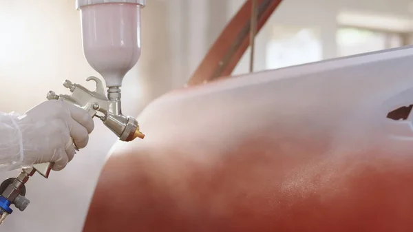 Otomobil boyacısı özel bölmede arabanın kapısına kırmızı boya sıkıyor, yavaş çekimde. Araba servisi atölyesinde araç parçaları boyuyorum. Araba üretim fabrikası.