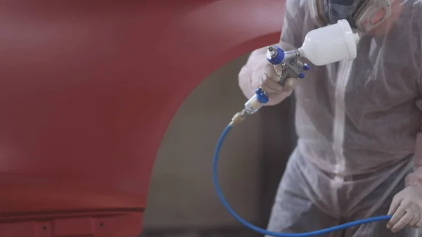 Red car in a paint chamber during repair work. Auto painting worker. Professional car painter is painting a body work. Male technician is air-painting cars door.