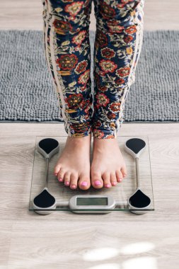 Closeup of barefoot woman using digital scales and checking her weight. Female feet step on floor scales. Concept of dieting, loosing weight and healthy lifestyle.