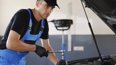 Male mechanic is working in car service. Hes using ratchet. Car mechanic using wrench to repair the engine, car service. Auto service. Man is working on an usual car maintenance.