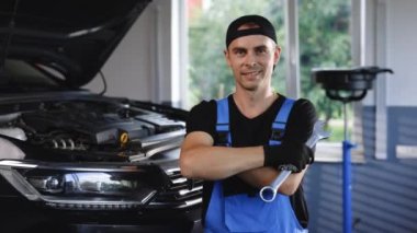 Portrait of european caucasian car mechanic in uniform with tools in his hands looks at the camera and laughs happily. Car service concept.
