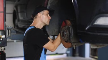 Car mechanic replacing car wheel brake shoes of lifted automobile at repair service station. Disc brake, caliper, lever system, traction, drive, shock absorber, boot.