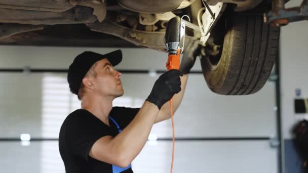 Caucasian male car mechanic checking car. Auto mechanic working underneath car lifting machine at the garage. Working in car repair shop and running small feminine business concept.