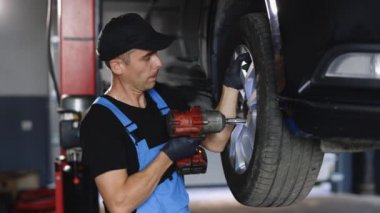 Car mechanic replacing car wheel of lifted automobile at repair service station. Assembly or dismantling of the wheels in the workshop. repair and maintenance of the car in service.