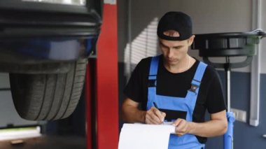 Mechanic inspects the car undercarriage way and makes a note on his inspection sheet. Automobile service, car mechanic. Car service employe inspect car. Modern workshop