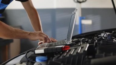 Computer diagnostics of the car. European car mechanic holds a digital device. Auto mechanic uses laptop while conducting diagnostics test. Modern car service.