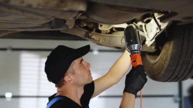 Caucasian car mechanic stands with led lamp looking at car parts to wipe the engine under the car on the overhaul to change the oil and maintain the engine in the garage.