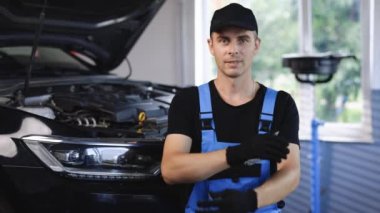 Portrait of car mechanic crossed arms in car workshop of service background . Concept: repair of machines, fault diagnosis, repair specialist, technical maintenance and on-board computer.