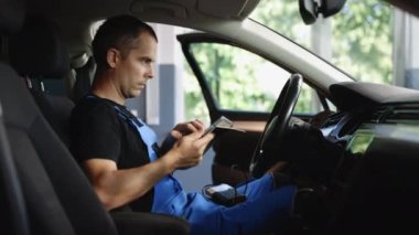 Mechanic using tablet pc at the repair garage service. Using digital tablet for car diagnostic. Interactive diagnostics software on an advanced computer.