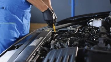 Close-up of automotive mechanic checks the oil level on the car engine dipstick. Car oil quality. Inspection of the engine and checking motor oil level. Man checks the car oil level with dipstick.