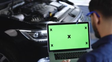 Car service mechanic uses laptop computer with green screen mock up chroma key car diagnostic software. Interactive diagnostics software on an advanced computer. Automotive electronic diagnostic app.