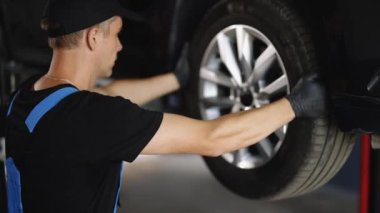 Experienced car service technician working at the garage. Mechanic repairing car at his workshop. Car on a lift in a specialized service Auto mechanic checking suspension of a lifted car.