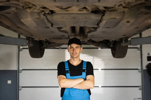 Mechanic man standing in front of the garage. Joyful young bearded man motor mechanic in overalls standing in workshop. Motor mechanic. Concept of small business, own business.