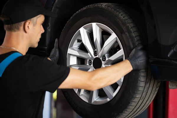 Experienced car service technician working at the garage. Mechanic repairing car at his workshop. Car on a lift in a specialized service Auto mechanic checking suspension of a lifted car.