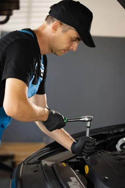 Car mechanic using wrench to repair the engine, car service. Auto service. Empowering male mechanic is working in car service. Man is working on an usual car maintenance. Hes using ratchet.