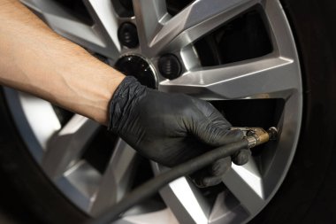 Mechanic inflating a car tire. Gas pumping of a car wheel. Car tire inflation. Car tire pressure check using air pressure guage.