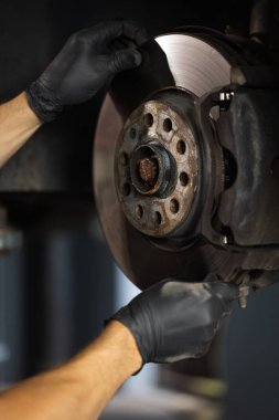Car mechanic in blue overalls replacing car wheel brake shoes of lifted automobile ac repair service station. Mechanic repairing car at his workshop. Auto mechanic checking vehicle.