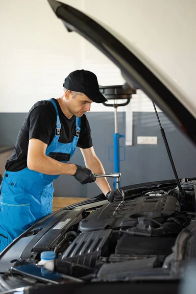 Male mechanic is working in car service. Man is working on an usual car maintenance. Hes using ratchet. Car mechanic using wrench to repair the engine, car service. Auto service.
