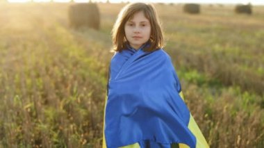 Üzgün Ukraynalı bir kızın portresi Ukrayna bayrağıyla günbatımı gökyüzüne karşı tarlanın ortasında duruyor. Ukrayna bayrağını tutan 8 yaşında bir kız. Ukrayna 'da savaş. Ukrayna 'ya Destek