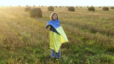 Gökyüzünde mavi-sarı bir bayrak taşıyan Ukraynalı bir kız. Ukrayna 'da savaş. Ukrayna Bağımsızlık Günü. Ukraynalı bir kızın portresi Ukrayna bayrağıyla tarlanın ortasında gün batımına karşı duruyor.