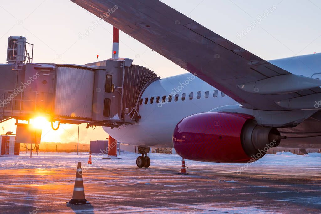 Close-up passenger jet plane near the boarding gate on the background of sunset in winter