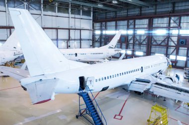 Beyaz yolcu uçakları hangarda. Jet uçakları bakım altında. Uçuş işlemleri için mekanik sistemler denetleniyor