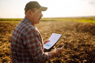 Çiftçi bazı haritaları izliyor ve toprağın kalitesini kontrol ediyor. Tarım, bahçıvanlık, iş veya ekoloji kavramı.