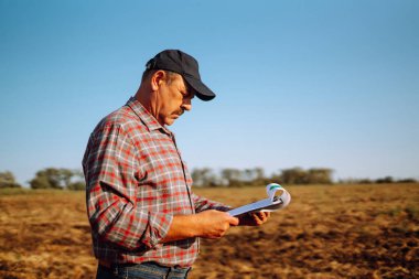 Çiftçi bazı haritaları izliyor ve toprağın kalitesini kontrol ediyor. Tarım, bahçıvanlık, iş veya ekoloji kavramı.