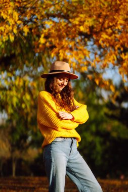 Parkta yürüyen şık bir kadın, sarı süveter ve şirin bir şapka giyiyor. Moda, tarz kavramı. İnsanlar, rahatlama ve tatil kavramı.