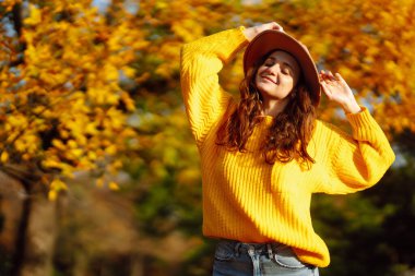 Parkta yürüyen şık bir kadın, sarı süveter ve şirin bir şapka giyiyor. Moda, tarz kavramı. İnsanlar, rahatlama ve tatil kavramı.
