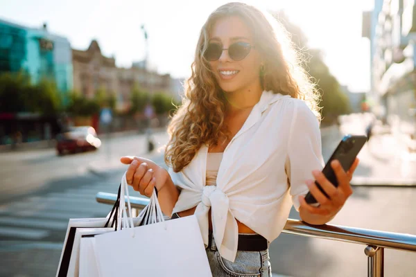 Młoda Kobieta Korzystająca Telefonu Trzymająca Torby Zakupy Stojąca Zewnątrz Wybierająca — Zdjęcie stockowe