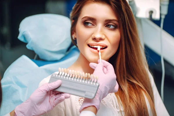 歯の色のサンプルを持つ若い女性 日陰ガイドを使用してインプラントの色合いを一致させます 歯科における歯のホワイトニングの準備 — ストック写真