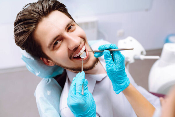 Young man at the dentist's chair during a dental procedure. Overview of dental caries prevention. Dentist examining patient's teeth in modern clinic. Healthy teeth and medicine concept.