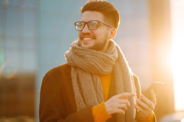 Hat bağlantısı. Elinde akıllı telefon olan paltolu genç bir adam sokakta yürüyor. Şehir geçmişinde modern saç stili olan sakallı genç adam cep telefonuyla yazı yazıyor.. 
