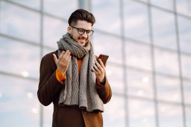 Hat bağlantısı. Elinde akıllı telefon olan paltolu genç bir adam sokakta yürüyor. Şehir geçmişinde modern saç stili olan sakallı genç adam cep telefonuyla yazı yazıyor.. 