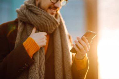 Hat bağlantısı. Elinde akıllı telefon olan paltolu genç bir adam sokakta yürüyor. Şehir geçmişinde modern saç stili olan sakallı genç adam cep telefonuyla yazı yazıyor.. 