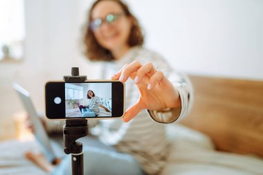 Video blogu. Genç bir kadın kameraya bakıyor ve video blogu yönetirken hikayesini anlatıyor. Vlogger telefon kullanarak çevrimiçi yayın yapıyor. Sosyal medya, instagram, evde kalıp karantina.