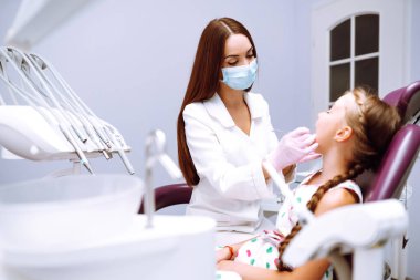 Pediatrik stomatolojide muayeneden sonra pediatrik dişçiyle konuşurken gülümseyen sevimli küçük kız. Erken müdahale, ağız hijyeni ve süt diş bakımı.