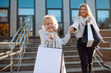 Alışveriş torbalarıyla şehir caddesinde yürüyen genç bir anne ve sevimli bir çocuk. Kara Cuma. Tüketim, satış, indirimler, yaşam tarzı konsepti.