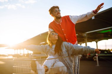 Pozitif erkek ve kadın eğleniyor ve alışveriş arabasına biniyor. İki genç arkadaş alışverişe gidiyor. Kara Cuma. Tüketim, satış, indirimler, yaşam tarzı konsepti.