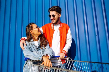 Pozitif erkek ve kadın eğleniyor ve alışveriş arabasına biniyor. İki genç arkadaş alışverişe gidiyor. Kara Cuma. Tüketim, satış, indirimler, yaşam tarzı konsepti.