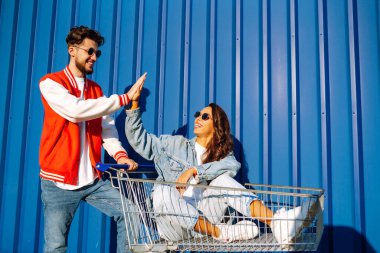 Pozitif erkek ve kadın eğleniyor ve alışveriş arabasına biniyor. İki genç arkadaş alışverişe gidiyor. Kara Cuma. Tüketim, satış, indirimler, yaşam tarzı konsepti.