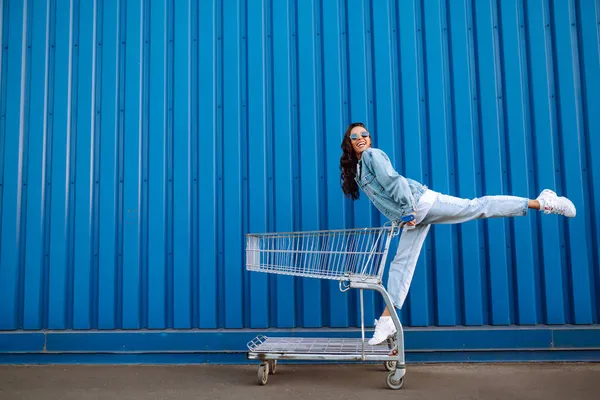 Alışveriş Arabalı Genç Bir Kadın Renk Duvarının Yanında Eğleniyor Gülümseyen — Stok fotoğraf