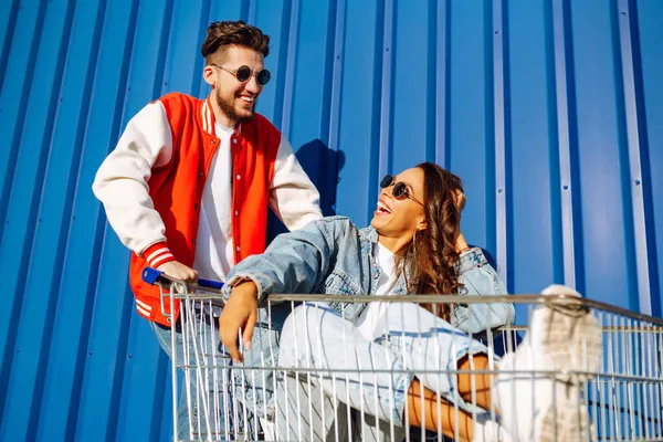 Pozitif erkek ve kadın eğleniyor ve alışveriş arabasına biniyor. İki genç arkadaş alışverişe gidiyor. Kara Cuma. Tüketim, satış, indirimler, yaşam tarzı konsepti.