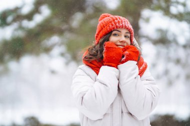 Kar parkında poz veren kırmızı şapkalı, kışın gülümseyen kadın. Soğuk hava. Kış modası, tatiller, dinlenme, seyahat konsepti.