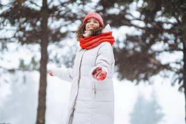 Kar parkında poz veren kırmızı şapkalı, kışın gülümseyen kadın. Soğuk hava. Kış modası, tatiller, dinlenme, seyahat konsepti.