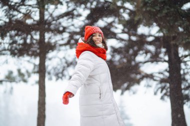 Kar parkında poz veren kırmızı şapkalı, kışın gülümseyen kadın. Soğuk hava. Kış modası, tatiller, dinlenme, seyahat konsepti.